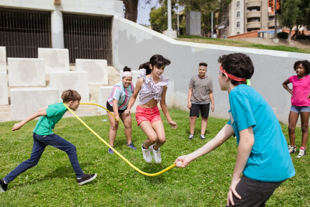 A group of kids jump rope on a patch of grass. This article covers how summer camps in Miami can offer the perfect environment for children to take social risks and develop essential skills.