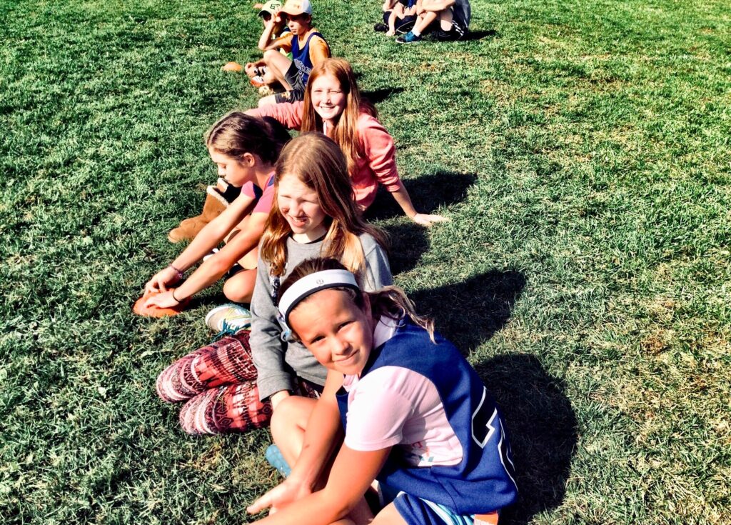 This article covers not just one, summer camp in Miami, but many, providing you with all the information you need to make the best choice for your little ones. In the photo are a group of kids sit in a line on a field of grass.